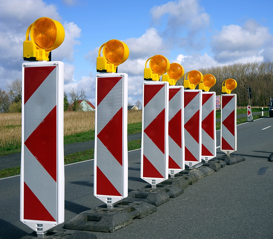 Warnbaken mit Streifen in Rot und Weiß und Blinkleuchten in Gelb an einer Baustelle